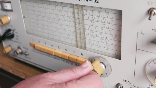 A person hand turns a yellow dial to adjust the tuning frequency on an old analog signal generator. Concept of retro technology, scientific measurement, and vintage electronic lab equipment.