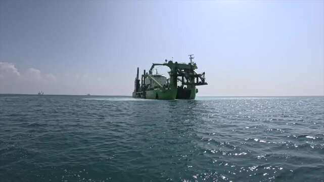 Large cutter suction dredger operating offshore in tropical waters. Industrial dredging vessel performing marine excavation and seabed maintenance under clear skies.