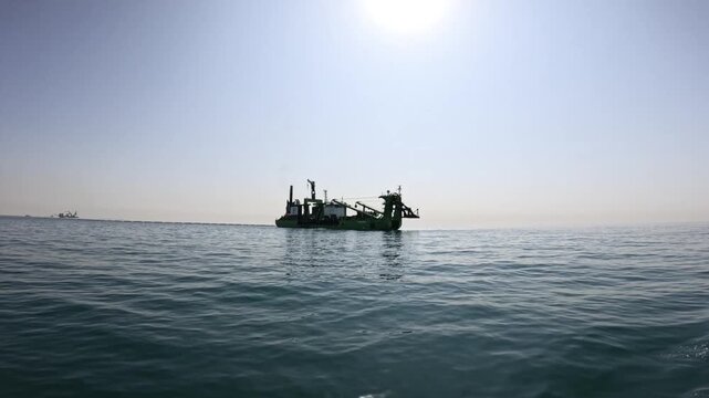 Large cutter suction dredger in slowmotion operating offshore in tropical waters. Industrial dredging vessel performing marine excavation and seabed maintenance under clear skies.
