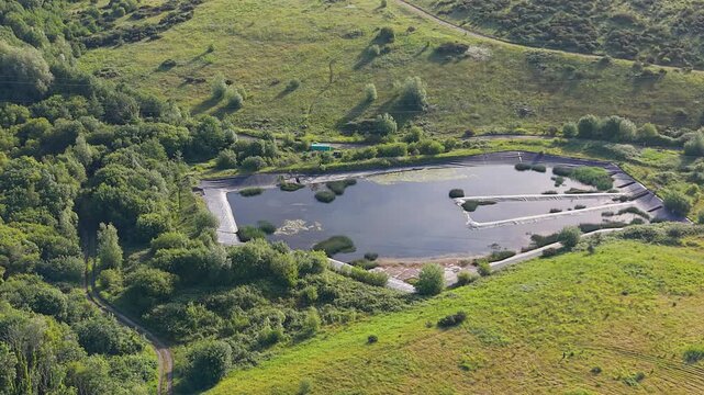 Sideways Aerial of Waterlogged Old Landfill Site with Reinforced Polyethylene Cover to suppress odours, control pests and stop rain turning the waste into contaminated water. South Wales, UK. 4K.