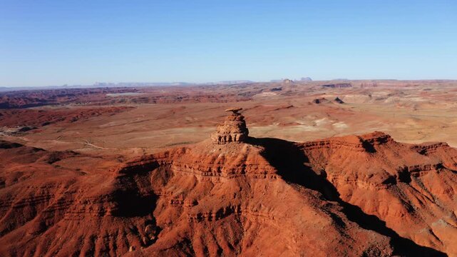 Wide aerial drone shot of Mexican Hat Rock in Utah showcasing desert landscape nearby.