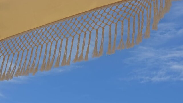 Beautiful 4K low-angle shot of white fringed macrame umbrellas at a luxury beach resort. Features an organized row of sunbeds, tropical palm trees, and a clear blue sky.