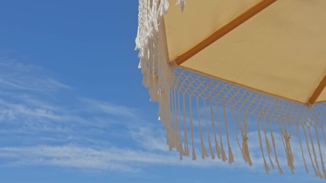 Beautiful 4K low-angle shot of white fringed macrame umbrellas at a luxury beach resort. Features an organized row of sunbeds, tropical palm trees, and a clear blue sky.