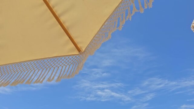 Beautiful 4K low-angle shot of white fringed macrame umbrellas at a luxury beach resort. Features an organized row of sunbeds, tropical palm trees, and a clear blue sky.