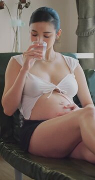 Healthy pregnant woman drinking clean water for hydration at home.