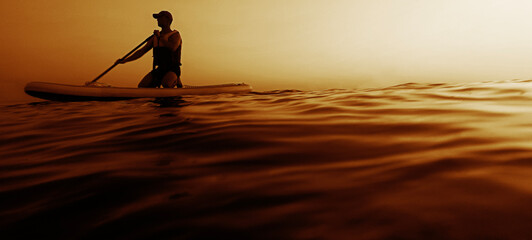 black silhouette of male man stands on a SUP board Floats down sea at sunset. Sport. Aquatic activities ocean watersport on ocean stand up paddleboard canoe Active summer standing person with paddle © Maxim Chuev