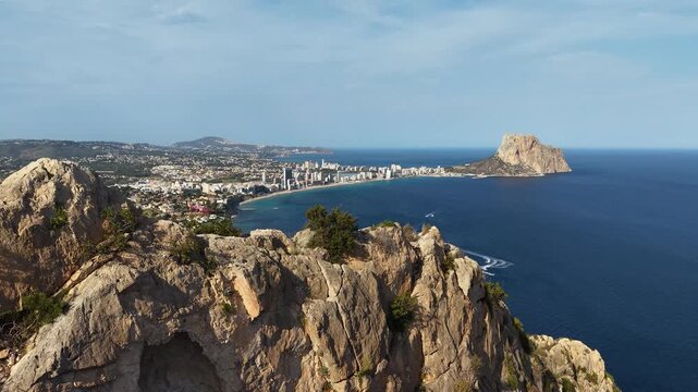 Drone aerial view from Morro de Toix overlooking Calpe, Spain with the Mediterranean coastline, sandy beach, and iconic Pe&ntilde;&oacute;n de Ifach rising above the sea