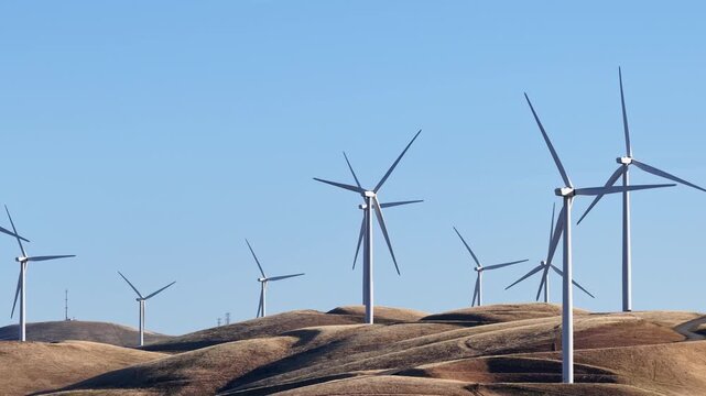 Golden rolling hills covered with a large wind farm generating sustainable and renewable energy under a clear blue sky in Altamont Pass, California, a landmark for clean power production