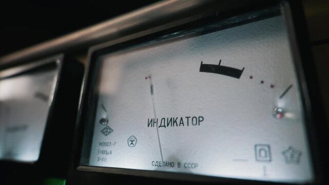 A close-up view of a vintage analog VU meter displaying audio levels on a retro amplifier. The dial features the Russian text for indicator and measures sound levels in a studio setting.