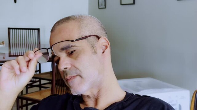 Close-up of a mature man taking off reading glasses to gesture, symbolizing focus, concentration, aging vision, and presbyopia