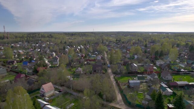 Drone flies low above a spring rural village with small houses garden roads scattered trees and forest horizon for countryside living and residential landscape themes