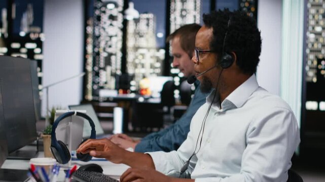 Startup helpdesk system administrator in office speaking in headset microphone, responding to service alerts. IT professional doing tech support, helping users across remote infrastructure.