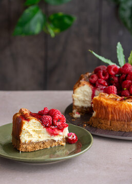A single slice of baked cheesecake topped with raspberry sauce and fresh berries, with the remaining cake in the background.