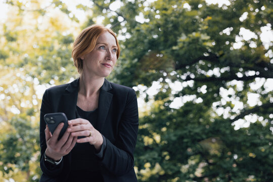 Professional Woman Using Phone looking at nature through her window