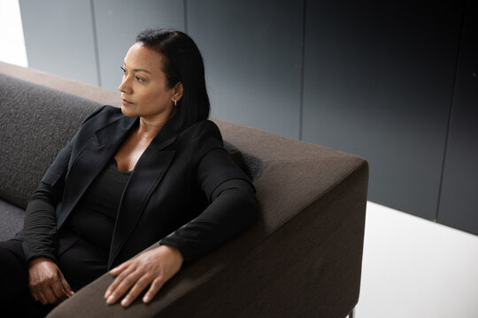 Focused woman in professional attire seated on couch