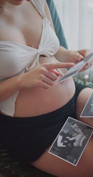 Close up of a pregnant woman looking at ultrasound baby photos at home.