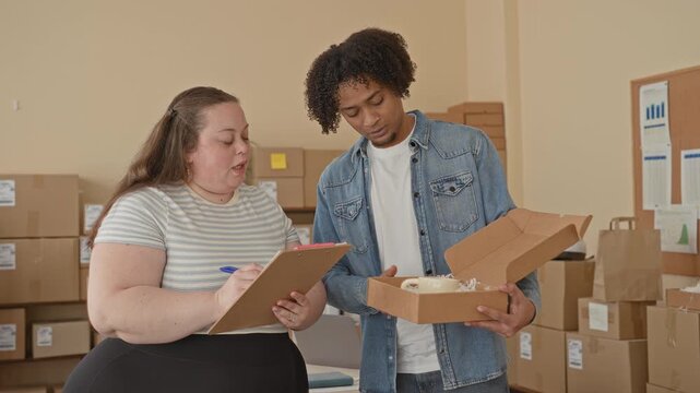 Woman inspects open box with hands holding a clipboard and pen while checking parcel labels in building; small business teamwork.