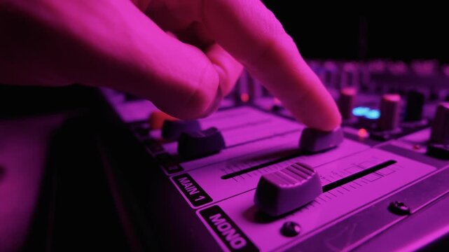 Close-up view of faders on an audio mixing board during a live performance or studio session. The equipment is illuminated by blue LED lights in a dark room. Labels show Main 1 and Mono.