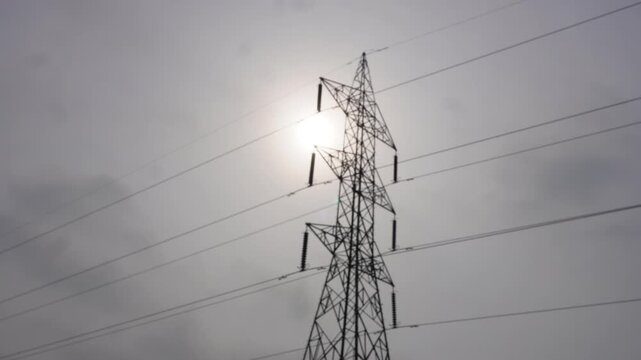 High voltage power tower silhouetted against sunset sun