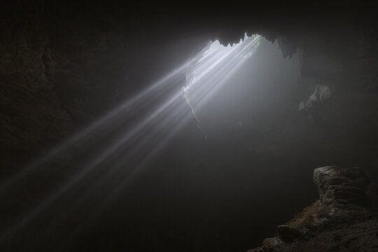 Light rays hitting limestone inside dark deep cave called Jomblang cave which is 60m deep an iconic adventure spot in Indonesia.