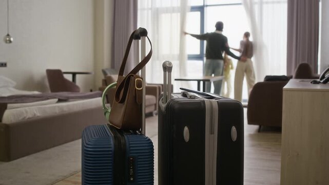 Establishing shot of suitcases standing in foreground with blurred family looking out of hotel window in background. Ideal for travel agencies, hospitality marketing, and family vacation campaigns