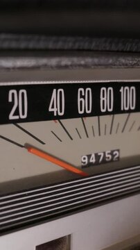 A vintage analog speedometer is shown in a close-up detail shot. The orange needle rests near zero on the black and white dial. Chrome accents and an odometer highlight the classic dashboard design