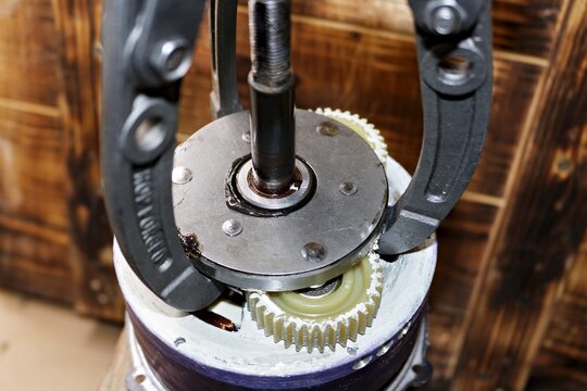 Three-jaw gear puller removing an overrunning clutch from a geared electric motor hub, performing DIY maintenance and repair of an e-bike motor assembly in a home workshop