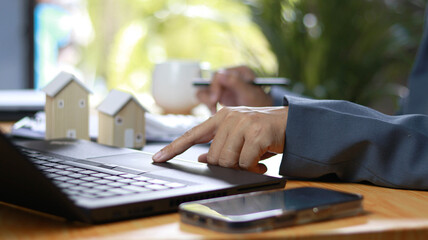 Business professional using laptop and smartphone with miniature house models on desk, representing...