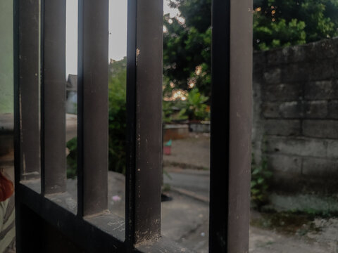 A close-up photograph of a metal gate with vertical bars in sharp focus, creating a strong geometric composition