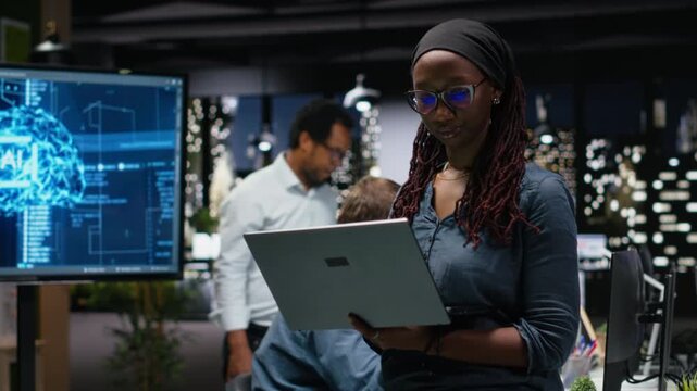 Female technician in office using laptop, working to fix bugs in AI system. Woman troubleshooting neural network errors with notebook in tech agency workplace.
