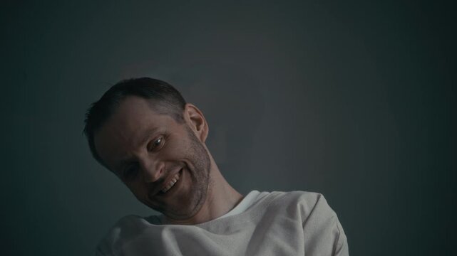 Chest up of middle aged Caucasian man wearing straitjacket laughing hysterically and smiling maniacally in psychiatric hospital clinic. Ideal for mental health awareness campaigns or horror films