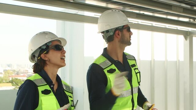 Engineers with safety vest and helmet work with electrical instrument on photovoltaic solar panels. Technicians discuss together. Woman use walkie talkie while man use multimeters to check solar power