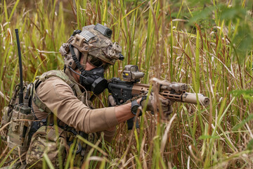 Fototapeta premium Soldier aims rifle in dense grass during training exercise in an outdoor setting
