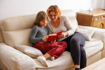 Obraz premium Mother and daughter reading a book while relaxing at home