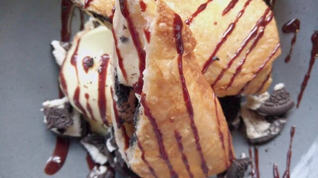 Closeup view of fried dessert served with ice cream chocolate sauce and cookie crumbs on ceramic plate with sweet topping and gourmet presentation