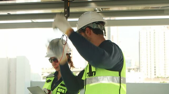 Engineers with safety vest and helmet work with electrical instrument on photovoltaic solar panels together. Male technician uses multimeters to check solar power, woman worker enter data into tablet