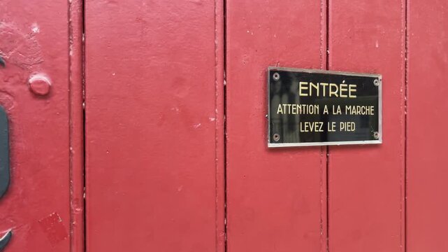 Red wooden entrance door with French warning sign on historic building facade