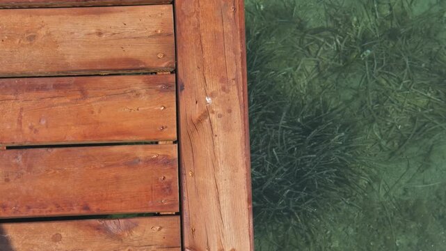 Top-down overhead shot of wooden pier edge over crystal clear Aegean water, seagrass visible on seabed below, beach club pier detail, Turkey