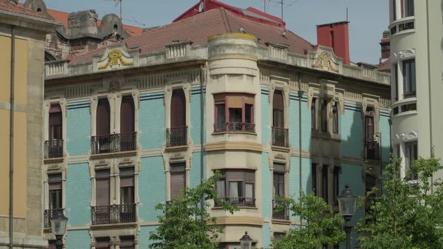 Medium shot of a beautiful traditional historic building with a light blue tile facade, ornate windows, and balconies at Plaza del Parchis in Gijon, Asturias, Spain.