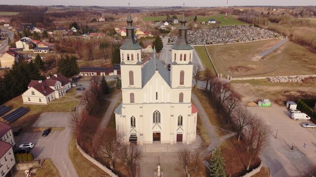 Sunlit Facade Midday Clarity Over Parish Piatnica, Crisp Shadows Reveal Texture Of Plaster And Masonry, Open Plaza And Cemetery Visible, Calm Aerial B Roll For Editorial And Stock Projects