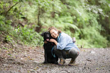 Obraz premium 森の中で愛犬と触れ合いながら笑顔を見せる女性のアウトドアライフカメラ目線