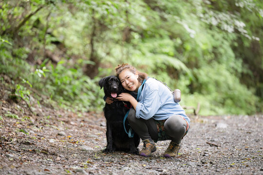 森の中で愛犬と触れ合いながら笑顔を見せる女性のアウトドアライフカメラ目線