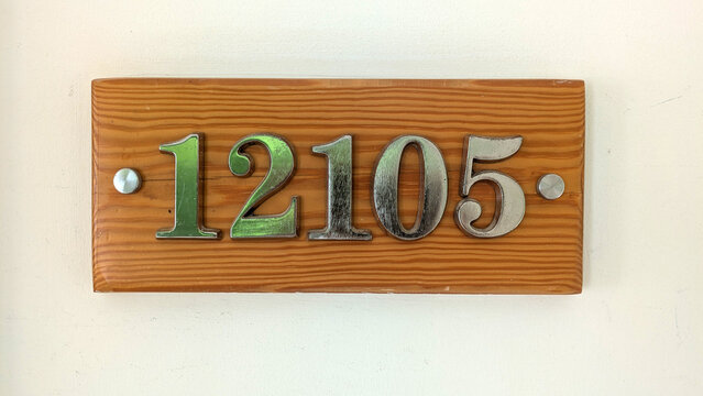 A wooden house number plaque with metallic digits mounted on a wall, displaying the number 12105.