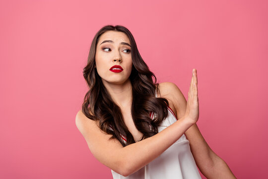 Glamorous stylish woman showing a dismissive gesture on a pink background, wearing a white dress and expressing defiance