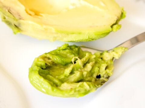 Close-up of a tablespoon filled with fresh, creamy mashed avocado over a seamless white background