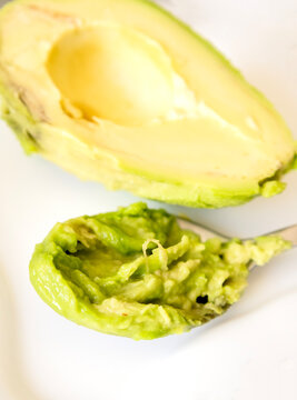 Close-up of a tablespoon filled with fresh, creamy mashed avocado over a seamless white background