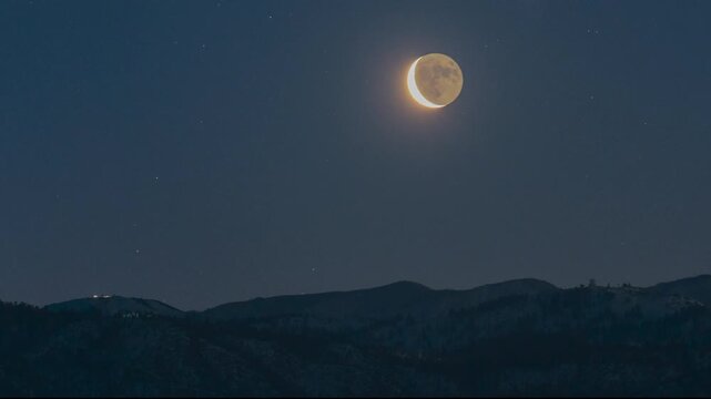 TIme lapse of a crescent moon rising over snowy mountains at dawn, wish snow cats grooming the slopes at Snow Valley, California, San Bernardino National Forest, California, filmed from Lake Arrowhead