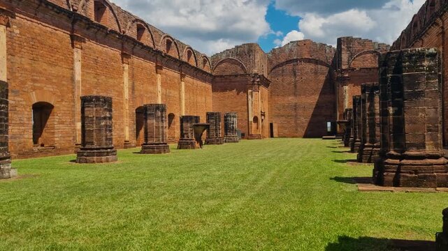 Sunlit view of the UNESCO-listed Jesuit Mission of Jes&uacute;s de Tavarang&uuml;&eacute; in Paraguay, with imposing brick ruins and tall columns standing over lush green grass