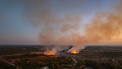 Fototapeta premium Aerial view of Smoke from burning fields spreads across the rural sky, slowly erasing the colors of sunset and turning a peaceful evening into a sign of environmental harm.