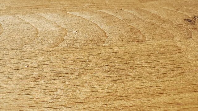 Close-up of a light wooden tabletop with visible grain, circular wipe marks, subtle scratches, warm tones, and natural timber surface texture.